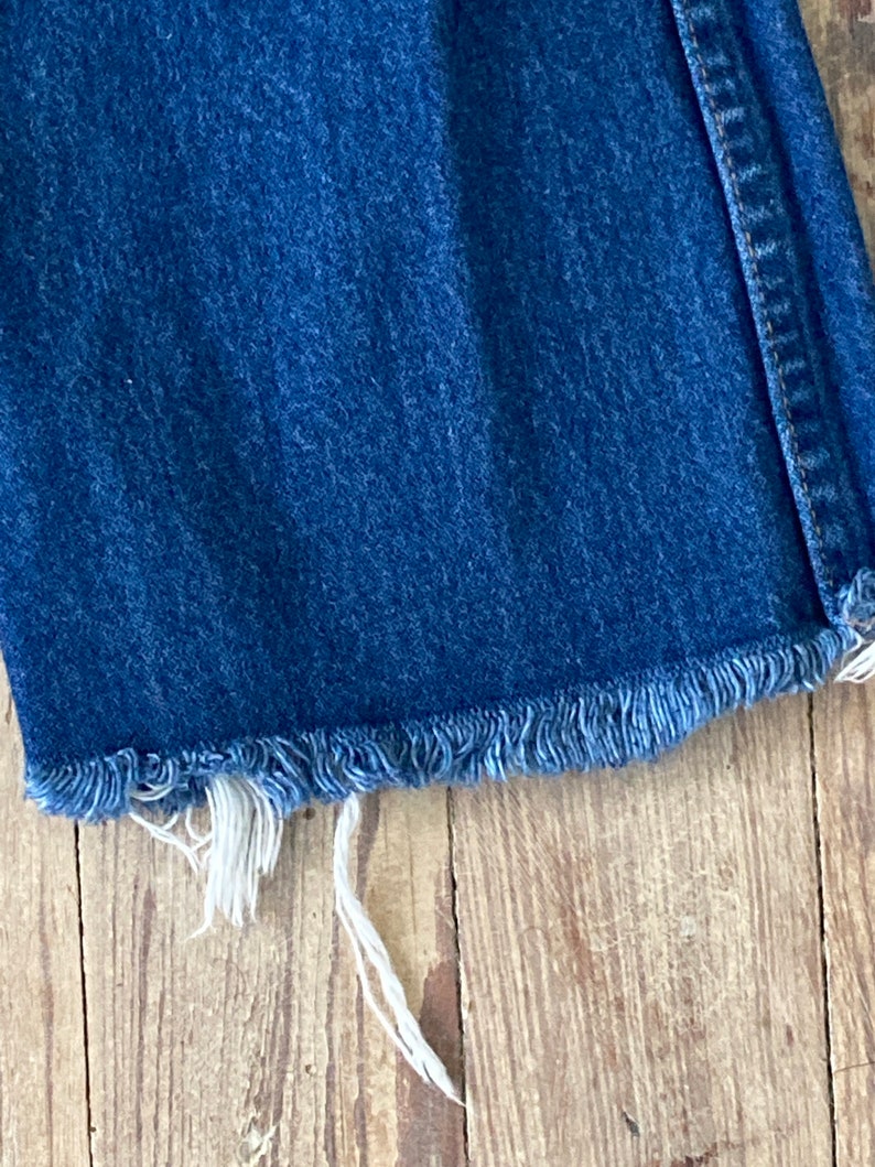 May include: Close-up of the frayed hem of a pair of blue denim jeans.