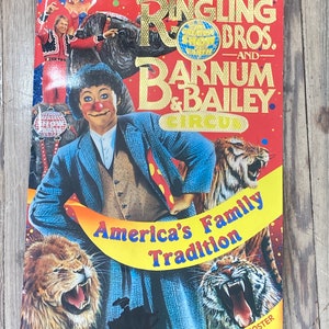 May include: A red, white, and gold poster advertising Ringling Bros. and Barnum & Bailey Circus. The poster features a clown with a red nose and a blue and white suit, a tiger, and a lion. The text on the poster reads "America's Family Tradition" and "Special Poster Inside".