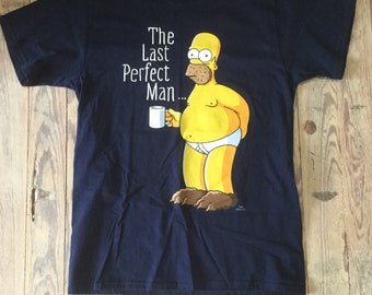 May include: A navy blue t-shirt featuring a cartoon image of Homer Simpson holding a mug. The text "The Last Perfect Man..." is printed on the shirt.