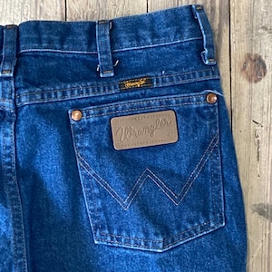 Puede incluir: Un par de pantalones vaqueros azules con un parche de cuero marrón en el bolsillo trasero que dice "Wrangler".