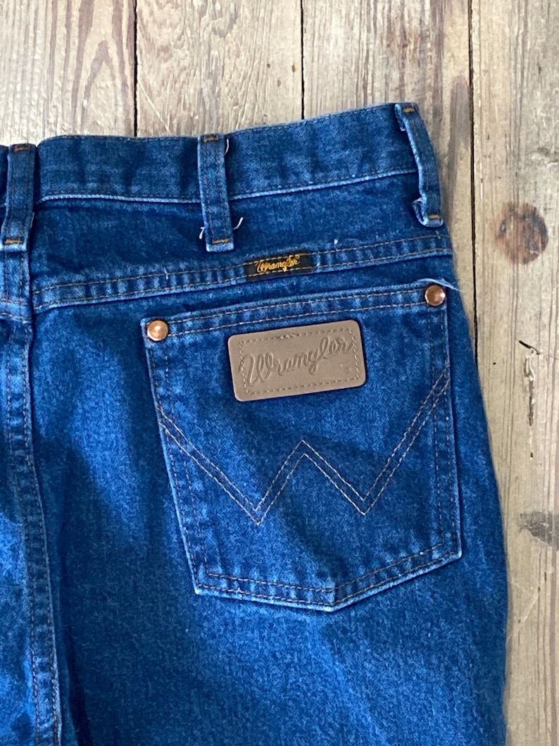 May include: A pair of blue denim jeans with a brown leather patch on the back pocket that says "Wrangler".