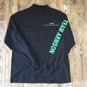 以下が含まれることがあります： モックネックと右袖に緑色の文字で「TEAM ARMISON」と「PTP PRO-TEAM PRODUCTS」と書かれた黒い長袖シャツ。