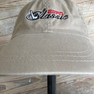 May include: A tan baseball cap with an embroidered logo that says "Classic" with a red "EST" and a hand gesture.