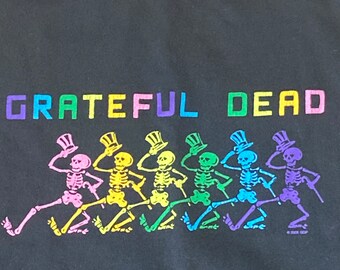 以下が含まれることがあります： レインボーカラーで「GRATEFUL DEAD」の文字が書かれた黒いTシャツ。Tシャツには、帽子をかぶって踊っている6人の骸骨が並んだグラフィックが描かれている。骸骨もレインボーカラーです。