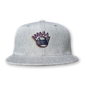 May include: A gray, flat-brimmed baseball cap with a colorful, cartoon-style face embroidered on the front. The face has a crown of spikes and a wide, toothy grin.