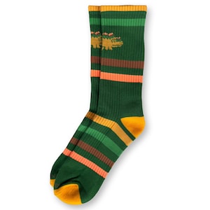 May include: Green crew socks with horizontal stripes in orange, brown, and green. The socks have yellow accents on the toe and heel, and a yellow alligator design near the top. The socks are made of a ribbed knit material.