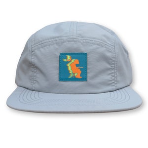 May include: A gray 5-panel cap with a blue patch featuring a stylized orange figure sitting on a chair with a crescent moon above the figure.