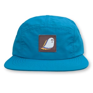 May include: A turquoise blue 5-panel cap with a brown patch featuring a white ghost with a rainbow outline.