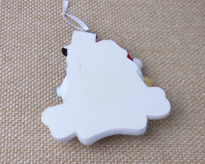 May include: White ceramic Christmas ornament shaped like a snowman with a red hat and a black top hat. The ornament has a white string for hanging.