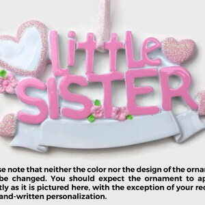 May include: Pink and white Christmas ornament with the words "little sister" and two hearts.