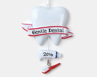 May include: White tooth-shaped Christmas ornament with a red ribbon that says "Gentle Dental" and a white tube of toothpaste with the year "2016" printed on it. A red toothbrush is attached to the bottom of the ornament.