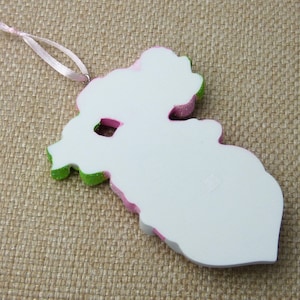 K&ouml;nnte beinhalten: Wei&szlig;er Weihnachtsbaumschmuck in Form einer Blume mit rosa und gr&uuml;nen Akzenten. Der Schmuck hat eine Schlaufe zum Aufh&auml;ngen.