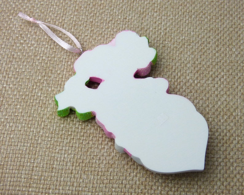 K&ouml;nnte beinhalten: Wei&szlig;er Weihnachtsbaumschmuck in Form einer Blume mit rosa und gr&uuml;nen Akzenten. Der Schmuck hat eine Schlaufe zum Aufh&auml;ngen.