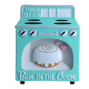 May include: A turquoise blue ceramic oven with a white door and a cinnamon roll inside. The oven has a timer set for and the words "Bun in the Oven" on the front.