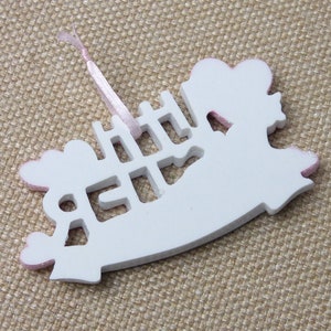 May include: White wooden ornament shaped like a rocking horse with pink glitter accents. The ornament has the word "Little" cut out in the center.