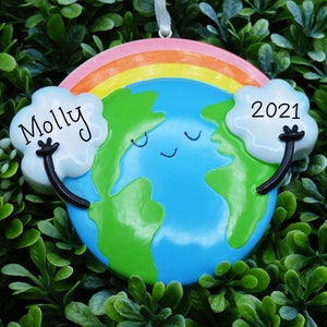 May include: A blue and green Earth ornament with a rainbow and clouds. The Earth has a smiling face and the clouds have the text "Molly" and "2021".