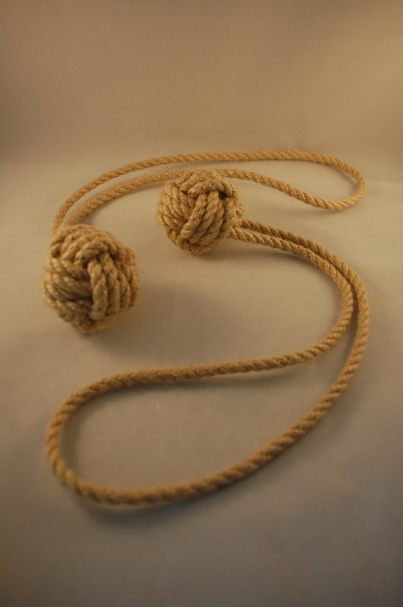 May include: A pair of beige rope tassels tied together with a long beige rope.