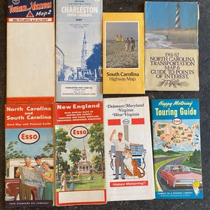 May include: A collection of vintage travel maps and guides, featuring various locations such as Charleston, South Carolina, and the Mid-Atlantic region. The maps showcase colorful illustrations and text, including the Esso logo and the phrase "Happy Motoring!"