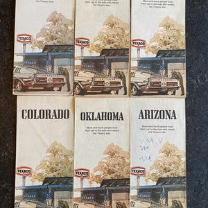 May include: A collection of vintage Texaco travel brochures. Each brochure features a classic car at a gas station, with the Texaco logo and the name of a state or country: New York, California, Mexico, Colorado, Oklahoma, and Arizona.