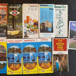 May include: A collection of vintage travel maps, including maps for Missouri, Kansas City, Nebraska, Minnesota, Kansas, and Arkansas. The maps feature colorful illustrations and text, showcasing various locations and attractions.