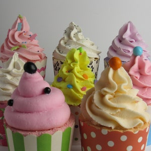 May include: An assortment of six cupcakes with colorful frosting and decorative toppings. The cupcakes are in various flavors, with pink, yellow, white, and lavender frosting. Each cupcake is in a decorative paper cup, with measurements in inches.