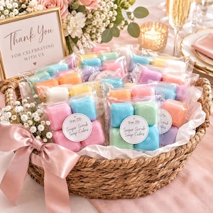 May include: A woven basket filled with individually wrapped pastel-colored sugar scrub soap cubes. Each clear plastic package features a round white label with the text Ginger Bliss Naturals Sugar Scrub Soap Cubes. A pink satin ribbon is tied to the basket handle.