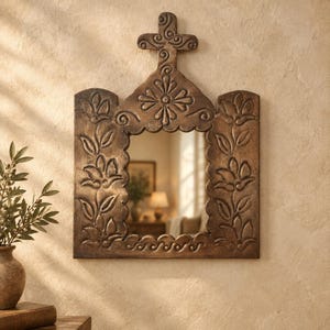 May include: A rectangular wall mirror with a dark brown finish and a carved wooden frame. The frame features embossed floral patterns, scalloped edges, and a cross-shaped top ornament with swirling scrollwork details throughout.