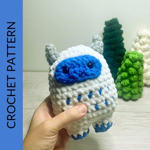 May include: A white crocheted yeti with blue eyes and a blue nose. The yeti is holding a small blue and white crocheted flower.