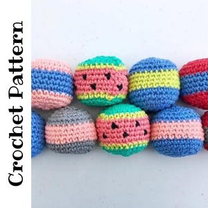 May include: A collection of small, spherical, multi-colored crochet balls arranged in rows. Some balls feature horizontal stripes in pink, blue, yellow, and gray, while others are green with black embroidered seed-like shapes. Text reads Crochet Pattern.