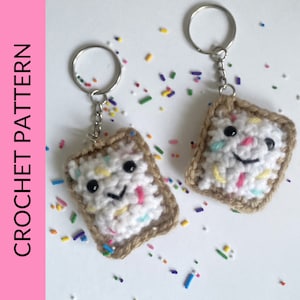 May include: Two crocheted keychains shaped like square toast with white frosting and colorful sprinkles. The keychains have black eyes and a smiling mouth.