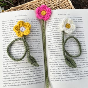 May include: Crocheted flower bookmarks in yellow, pink, and white, resting on an open book. The handmade bookmarks feature detailed flower designs with green stems and leaves, perfect for book lovers.