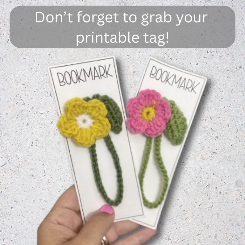 May include: Two handmade crochet flower bookmarks. One bookmark features a yellow flower with a white center, the other a pink flower with a yellow center. Both have green leaves and stems, and are attached to white cards labeled "BOOKMARK".