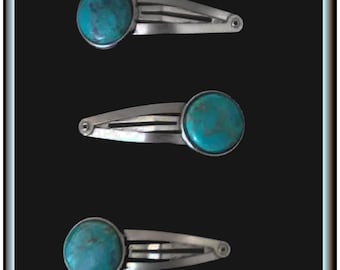 May include: Three silver-toned hair clips, each featuring a round, turquoise stone. The clips are arranged vertically against a black background. The turquoise stones have a mottled appearance, adding visual interest to the hair accessories.