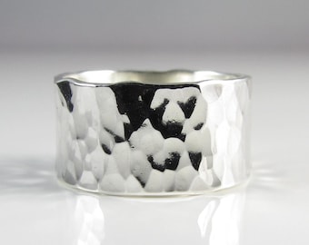 May include: A wide silver band ring with a hammered texture. The ring is made of sterling silver and has a polished finish.