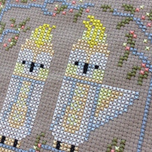 May include: Cross stitch pattern featuring two yellow-crested cockatoos perched on a branch with pink flowers.