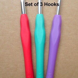 May include: Set of three crochet hooks with colored handles. The hooks are 6mm, 5.5mm, and 5mm. The handles are red, teal, and purple. The text "Set of 3 Hooks" is above the hooks.