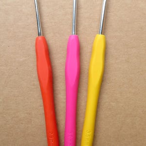 May include: Set of three crochet hooks with colorful handles. The handles are red, pink, and yellow. The text "Crochet Hooks Set of 3" is at the top. The hook sizes are 2.5mm, 3mm, and 3.5mm.