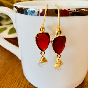 May include: A pair of gold earrings with red teardrop-shaped stones and white round stones hanging from them.