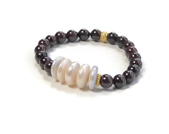 May include: A bracelet made with dark red garnet beads and a cluster of white pearl beads. The bracelet has a gold accent.