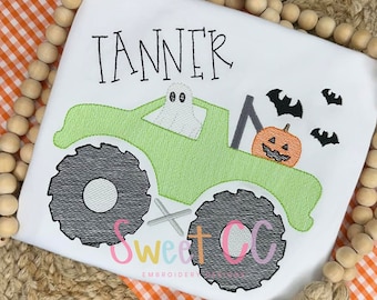 Op de afbeelding: Wit t-shirt met een groen monstertruckontwerp, met een spook, pompoen en vleermuizen. De naam "TANNER" is boven de truck geborduurd. Het shirt is versierd met de tekst "Sweet OC Embroidery Designs".