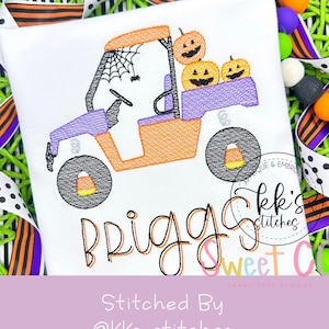 May include: White t-shirt with an embroidered Halloween design. The design features an orange and purple buggy carrying three carved pumpkins. A spider and web are above the buggy. The name "Briggs" is below the buggy.