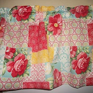 May include: A floral valance with a patchwork design. The valance features red roses on a light blue background, interspersed with yellow, red, and white patterned squares. The top edge is gathered, and the bottom edge is scalloped.