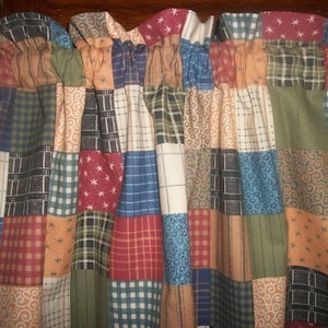 May include: A patchwork valance with a variety of fabric patterns and colors. The valance features squares of red, blue, green, and tan fabrics with plaid, floral, and star designs. The top of the valance is gathered and attached to a wooden rod.