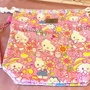 Pode incluir: Bolsa rosa com cord&atilde;o com um padr&atilde;o repetido de personagens Hello Kitty, flores e outras ilustra&ccedil;&otilde;es fofas. A bolsa tem um fecho de cord&atilde;o com uma corda branca e uma al&ccedil;a rosa. A bolsa &eacute; feita de um tecido macio estampado.