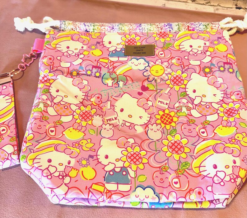 Pode incluir: Bolsa rosa com cord&atilde;o com um padr&atilde;o repetido de personagens Hello Kitty, flores e outras ilustra&ccedil;&otilde;es fofas. A bolsa tem um fecho de cord&atilde;o com uma corda branca e uma al&ccedil;a rosa. A bolsa &eacute; feita de um tecido macio estampado.