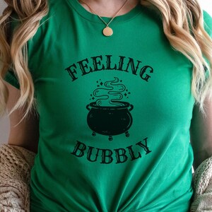May include: A green t-shirt with a black graphic of a cauldron with steam coming out of it. The text "Feeling Bubbly" is printed on the shirt.