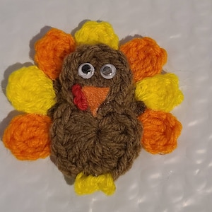 May include: A handmade turkey decoration made of brown yarn with googly eyes, an orange beak, and a red wattle. The turkey has yellow and orange yarn feathers. A festive, handcrafted item for Thanksgiving or fall decor.