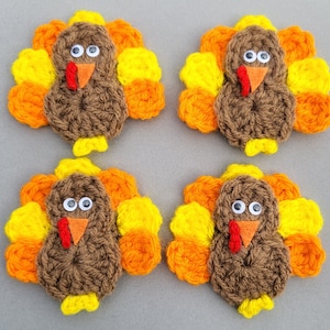 May include: Four handmade crochet turkey decorations. Each turkey has a brown body, a red wattle, an orange beak, and googly eyes. The tail feathers are yellow, orange, and yellow. The turkeys are arranged in a square.