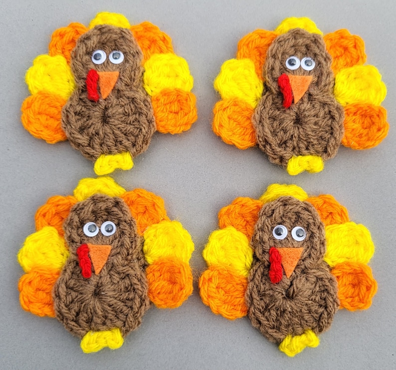 May include: Four handmade crochet turkey decorations. Each turkey has a brown body, a red wattle, an orange beak, and googly eyes. The tail feathers are yellow, orange, and yellow. The turkeys are arranged in a square.