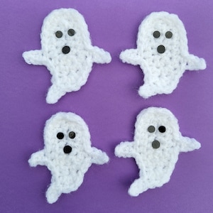 May include: Four handmade white crochet ghost appliques with black button eyes, arranged on a purple background. Each ghost has outstretched arms and a flowing bottom, perfect for Halloween crafts or decorations.